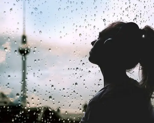 Junge Frau schaut durch ein verregnetes Fenster, im Hintergrund der Berliner Fernsehturm