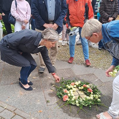 Dr. Ursula Schoen und Pfarrerin Andrea Köppen legen Blumen an verlegten Stolpersteinen ab