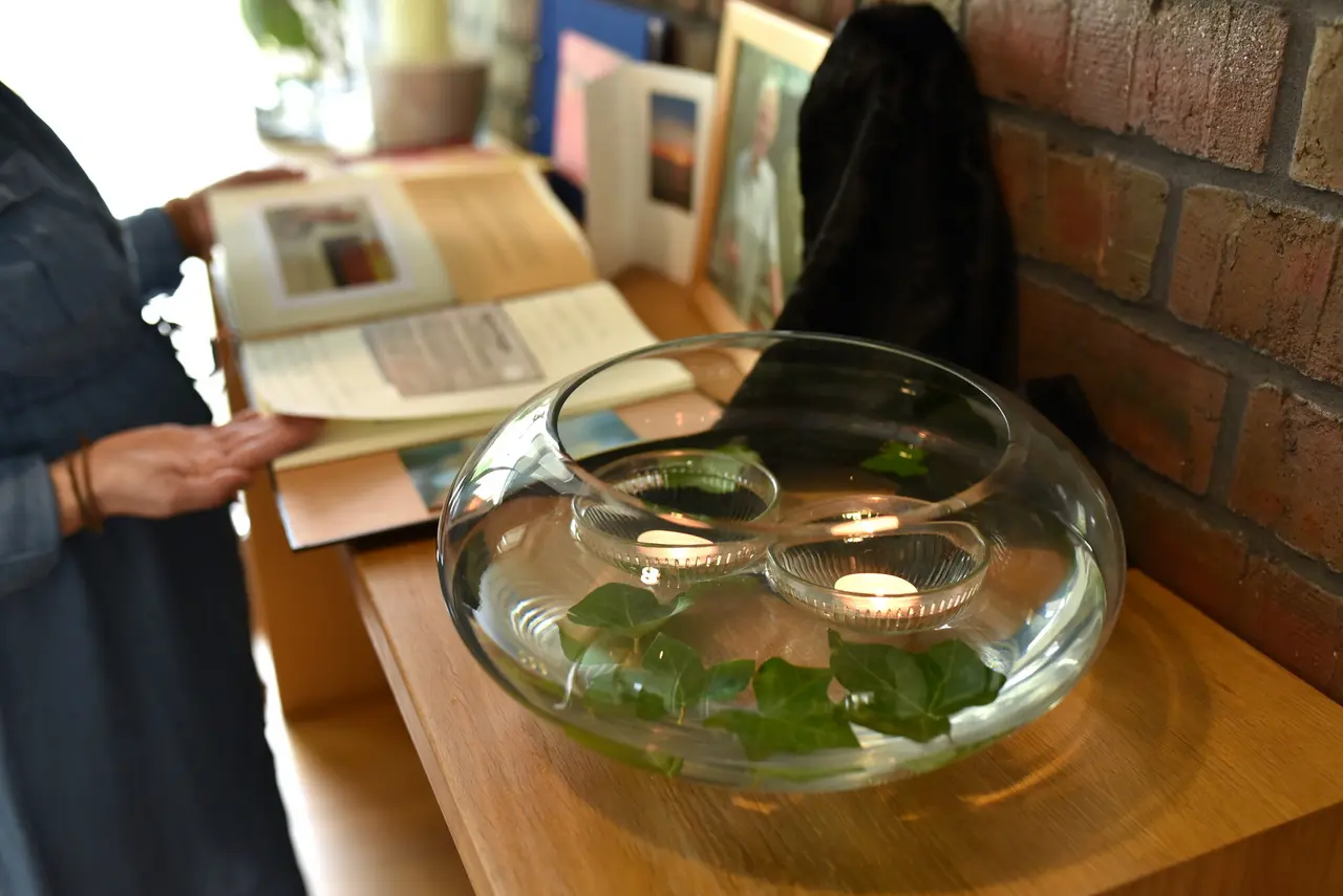 Auf einem Altar für eine Verstorbene im Hospiz steht eine mit Wasser gefüllte Vase, in der zwei Teelichter und Blätter schwimmen.