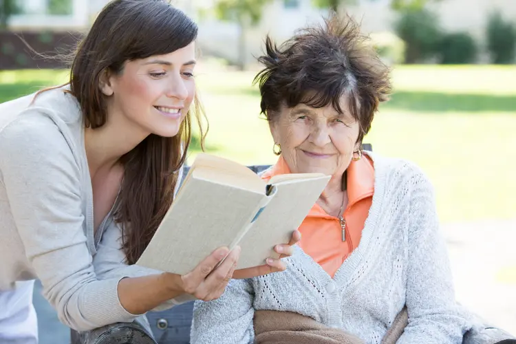 Junge Frau ließt Seniorin ein Buch vor